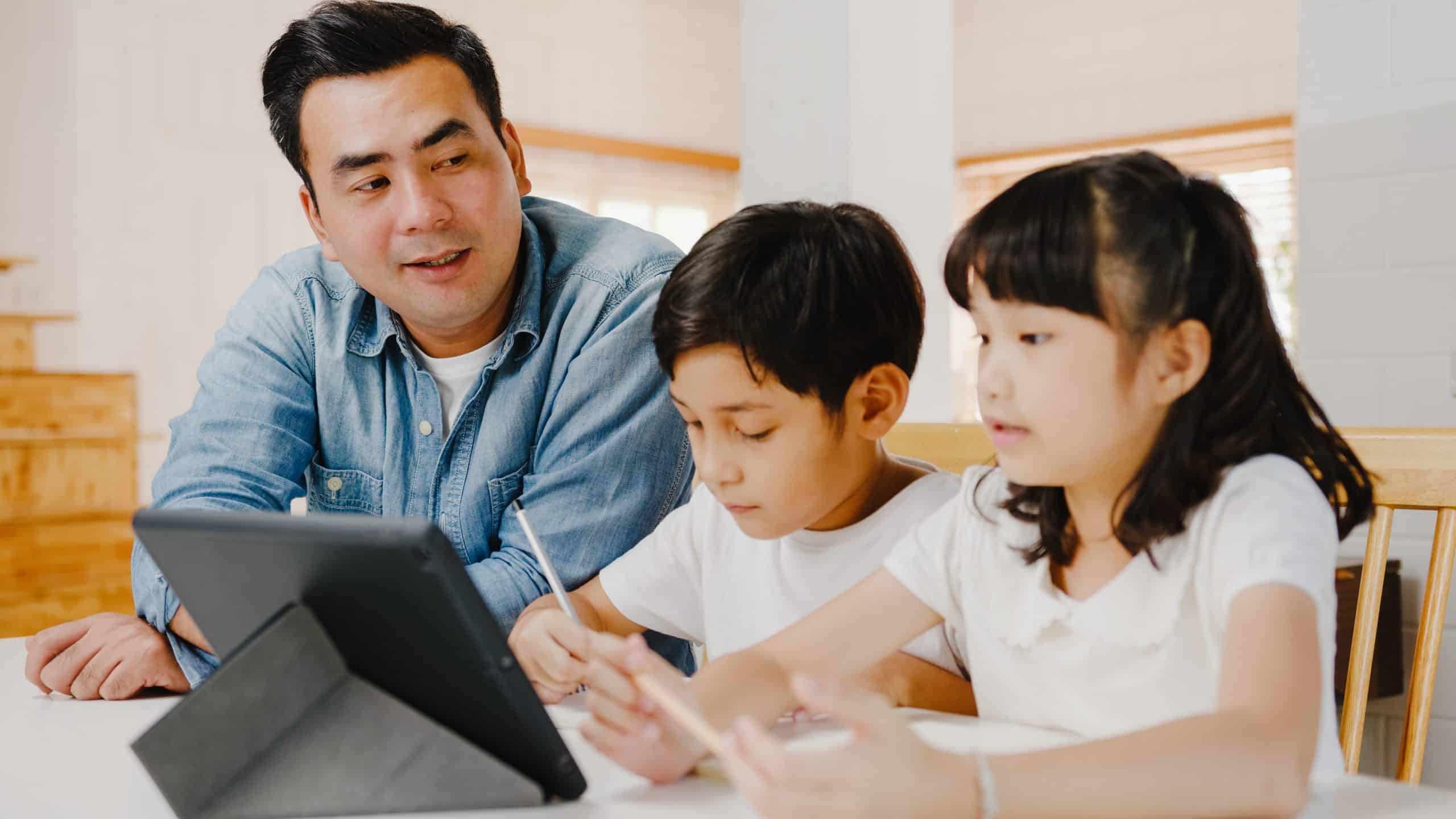 Father teaching children using digital tablet in living room at home.