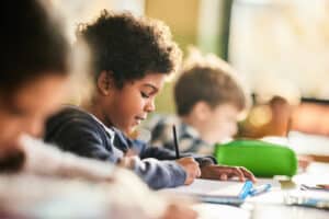 Smiling schoolboy writing on a class at elementary school