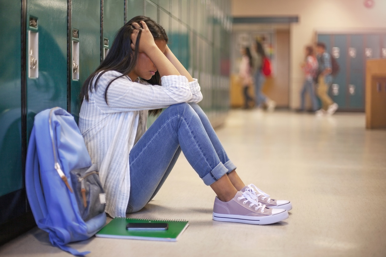 Frustrated teenage young woman female student with head in hands in hallway in school